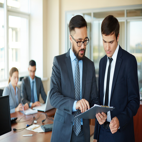 Confident businessman pointing at document while explaining his idea to his partner on background of their colleagues